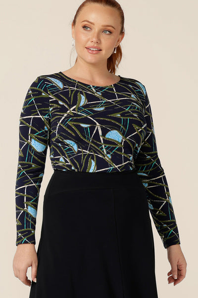 a size 12, curvy woman wears a long sleeve, boat neck top by Australian and New Zealand women's clothing brand, L&F. Featuring a blue, green and white print on a navy jersey base, this top is a great top for work and corporate wear.