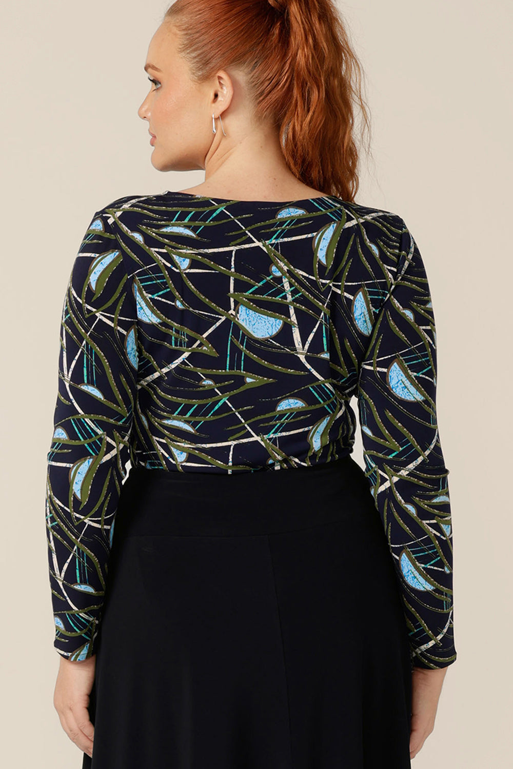 Back view of a size 12, curvy woman wearing a long sleeve, boat neck top by Australian and New Zealand women's clothing brand, L&F. Featuring a blue, green and white print on a navy jersey base, this top is available to shop Australia and New Zealand-wide in sizes 8 to 24.  