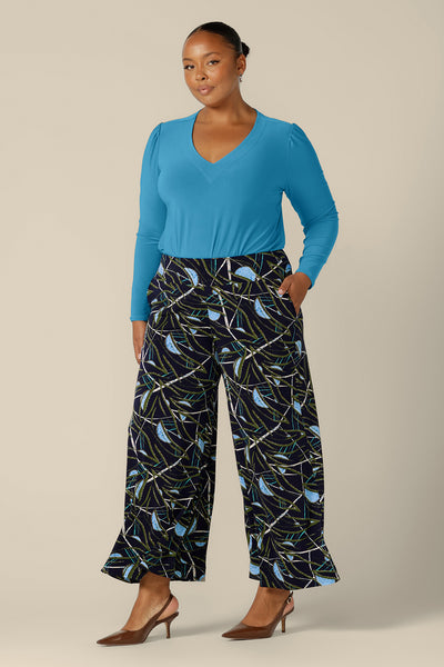 A plus size, size 18 woman wears a long sleeve, V-neck top in Opal blue jersey. Australian-made and shipping across Australia and New Zealand, this blue work top is worn with printed, wide-leg pants for workwear with personality.