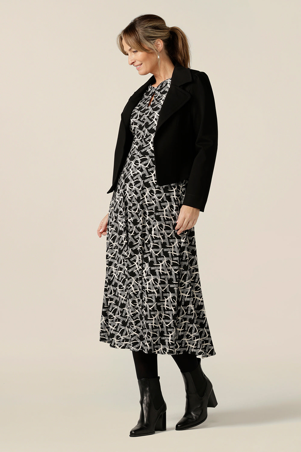 A size 10 woman wears a midi length, long sleeve dress with twisted keyhole detail with a black workwear jacket. Made by Australian and New Zealand women's clothing label, L&F in an inclusive size range of sizes 8 to 24.