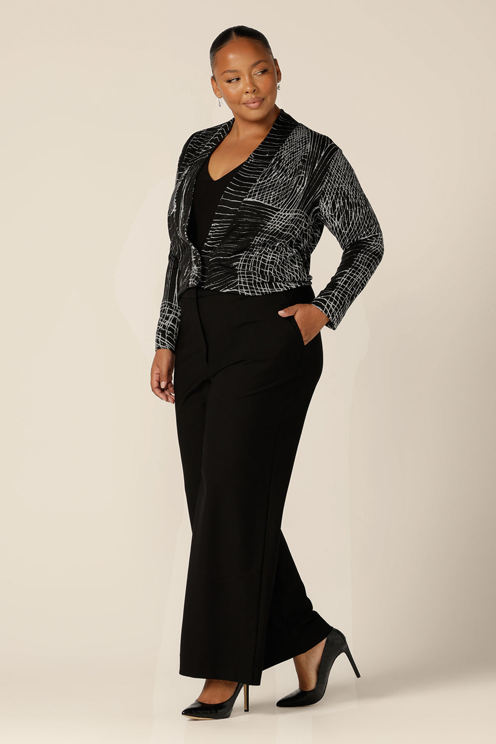 A blend of jacket and cardigan, this textured knit 'jacardi' is a great way to layer up for winter. Worn by a plus size, size 18 woman, this knit jacket is worn with a black V-neck top and tailored black pants for winter workwear style.