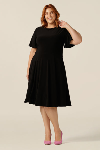 size 18, plus size woman wearing a reversible fixed wrap dress in black jersey. Worn reversed, she wears it as a boat-neck little black dress. Featuring short flutter sleeves, a knee length skirt and pockets, this dress can be worn for work wear or going-out dress style. Made in Australia by women's clothing label, Leina and Fleur