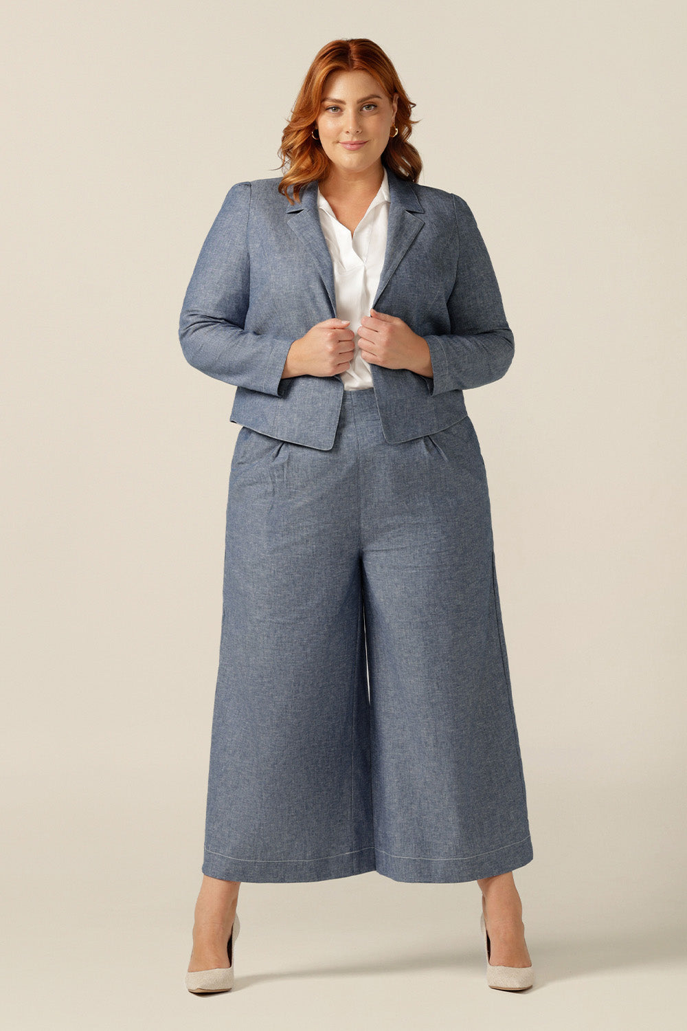 size 18 woman wearing a soft tailored jacket in cotton-linen blend Chambray fabric. The jacket is open-fronted and has long sleeves. This jacket is styled with a white shirt and matching Chambray tailored, cropped-length pants to give a work wear look. Jacket, shirt and pants are made in Australia for petite to plus size women.