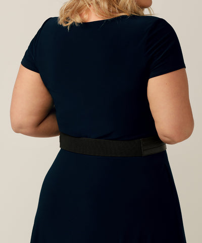 This black leather-look belt with a silver buckle is designed to fit around the waist and features a stretchy back for a comfortable fit. It comes in nine different sizes to accommodate various body shapes. In the photo, a plus-sized model is wearing the belt with corporate attire.