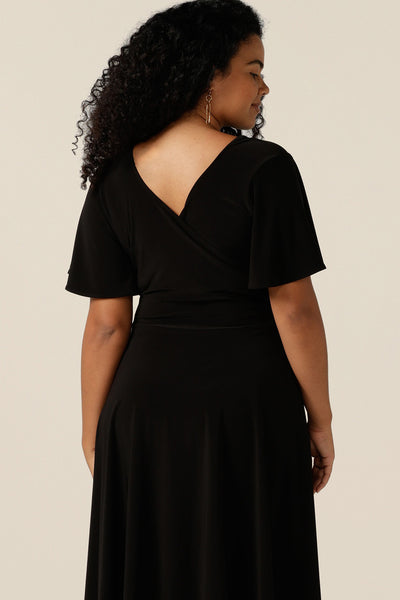 size 12, curvy woman wearing a reversible fixed wrap dress in black jersey. Worn reversed, as a boat neck dress, she styles as elegant jersey little black dress. Featuring short flutter sleeves, a knee length skirt and pockets, this dress can be worn for work wear or going-out dress style. Made in Australia by women's clothing label, Leina and Fleur