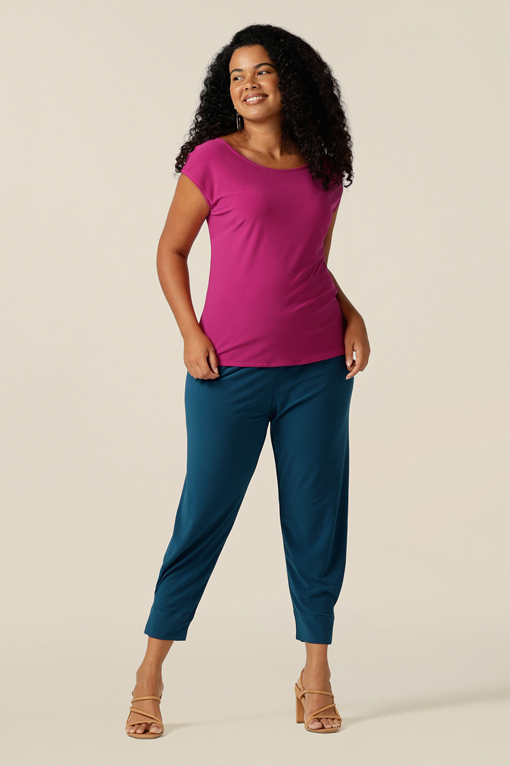 A size 12 woman wears a slim fit top with boat neckline and cap sleeves. In fuchsia pink stretch jersey, this top offer a comfortable slim fit for curvy women. The top is styled with a tapered leg jersey pant for a casual outfit.