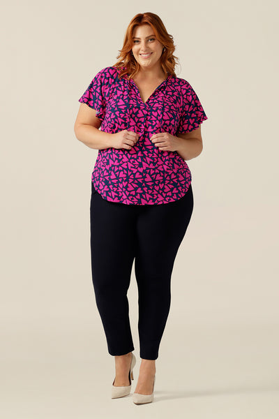 A plus size, size 18 woman wears a casual jersey top. The top has short raglan sleeves, a V-neckline and is printed with pink hearts for a Valentines Day fashion look. 