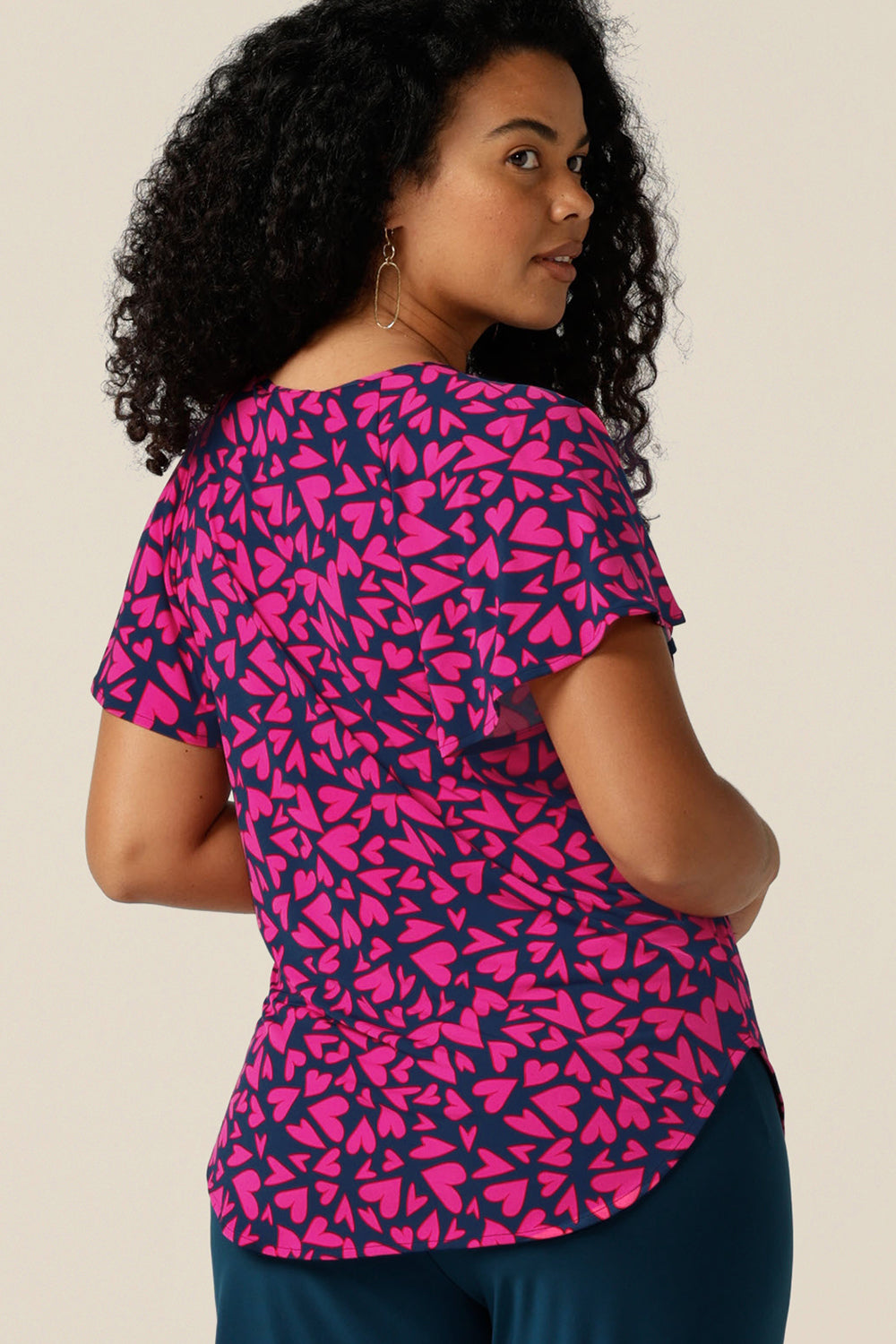 A size 12 curvy woman wears a V-neck short sleeve jersey top printed with pink hearts and designed and made in Australia.