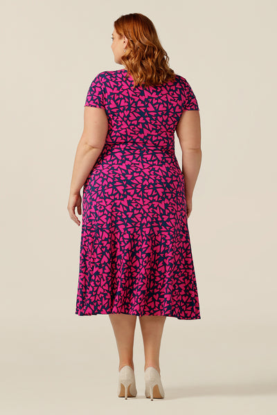 size 18 curvy woman wears a reversible jersey wrap dress. Worn with the crossover neckline to the front, this dress can be worn reversed with a boat neckline. This dress has short sleeves and a below-the-knee skirt with pockets. The dress is patterned with a pink heart print - perfect as a Valentines Day date-night dress or evening or occasionwear.