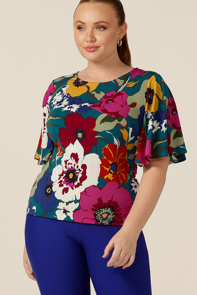 A curvy size 12 woman wears a round neck jersey top with short flutter sleeves. Made in Australia, this floral print top is made by Australian and New Zealand women's clothing brand, L&F in an inclusive 8-24 size range.