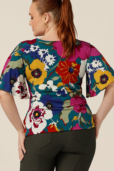 A curvy size 12 woman wears a round neck jersey top with short flutter sleeves. Australian-made, this floral print top is good for work or casual wear.