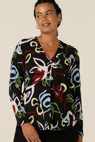 A size 12, curvy woman wears a V-neck jersey top with long sleeves and a shirttail hemline. Australian-made by Australia and New Zealand women's fashion brand, L&F this long sleeve top features black base print. This workwear top is worn with black trousers for easy office style.