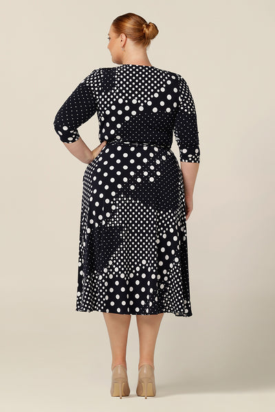 Back view of a jersey wrap dress with navy and white polka dot print, this is a great corporate wear dress. Featuring 3/4 sleeves and a full, midi length skirt, this wrap dress looks stylish on plus size and fuller figure women.