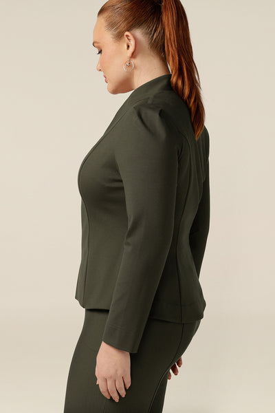 A size 12, curvy woman wears a tailored jacket with collarless V-neckline and zip fastening. In olive green ponte jersey, the stretch fabric makes for a comfortable workwear jacket.