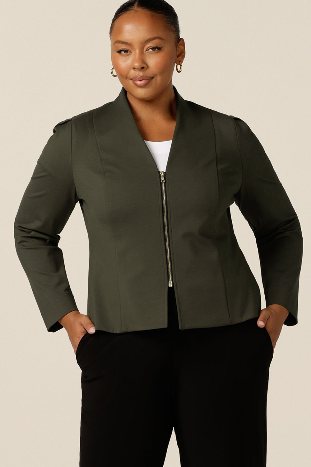 A size 18, fuller figure woman wears a tailored jacket with collarless V-neckline and zip fastening. In olive green ponte jersey, the stretch  fabric makes for a comfortable workwear jacket.