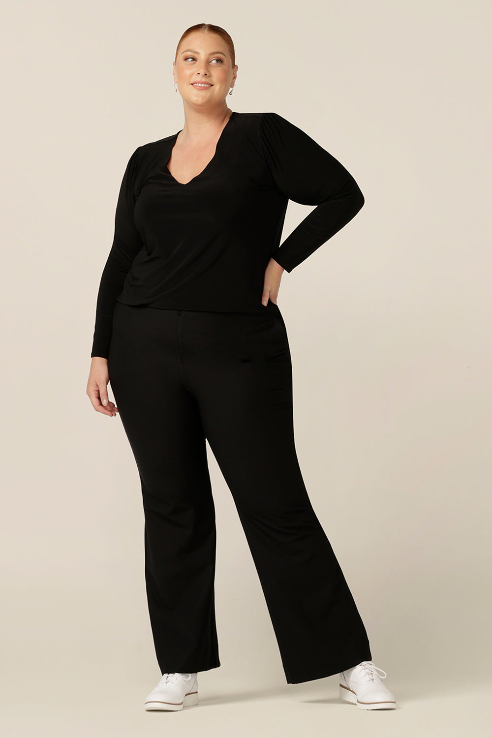 A size 18, fuller figure woman wears a long sleeve, V neck top in black jersey. Worn with black bootleg trousers and sneakers, this black top is styled for casual wear.  Comfortable and easy-to-wear, this classic women's top is made in Australia by Australia and New Zealand women's clothing label, L&F.