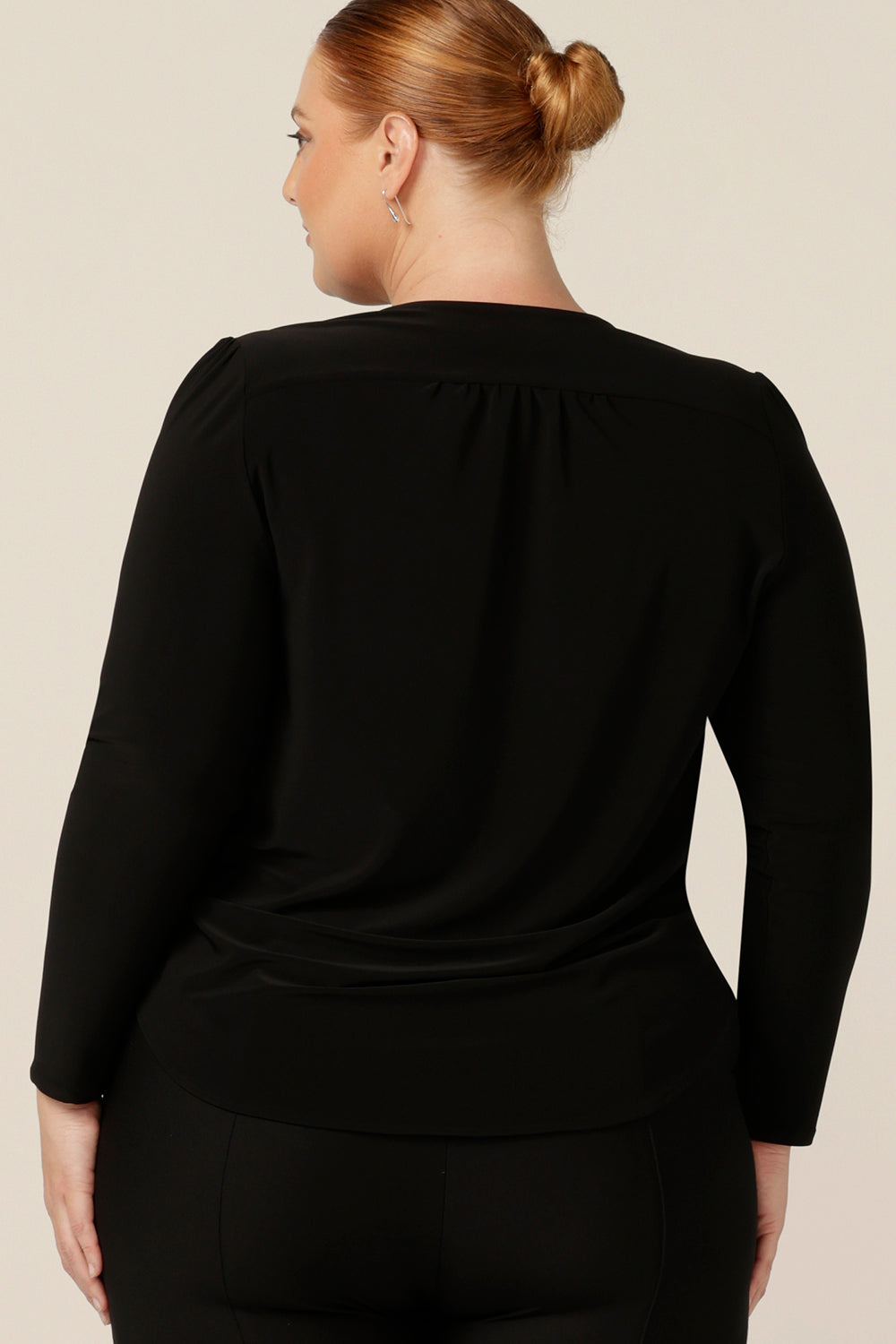Back view of a size 18, fuller figure woman wearing a long sleeve, V neck top in black jersey. A comfortable top for corporate or casual wear, this classic women's black top is made in Australia by Australia and New Zealand women's clothing label, elarroyoenterprises.