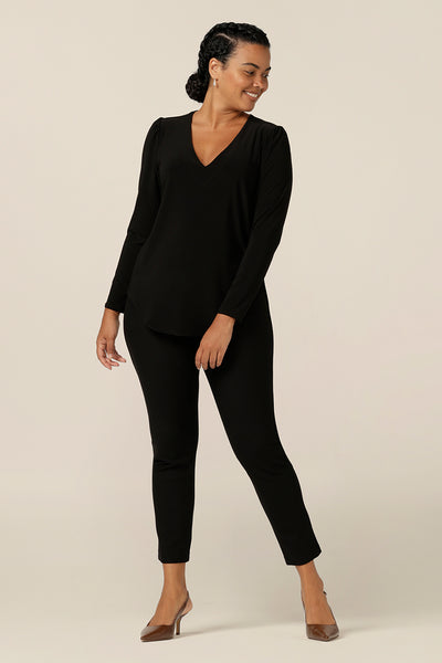 A size 12, curvy woman wears a long sleeve, V neck top in black jersey with slim leg black pants. A comfortable top for work or casual wear, this classic women's top is made in Australia by Australia and New Zealand women's clothing company, L&F.