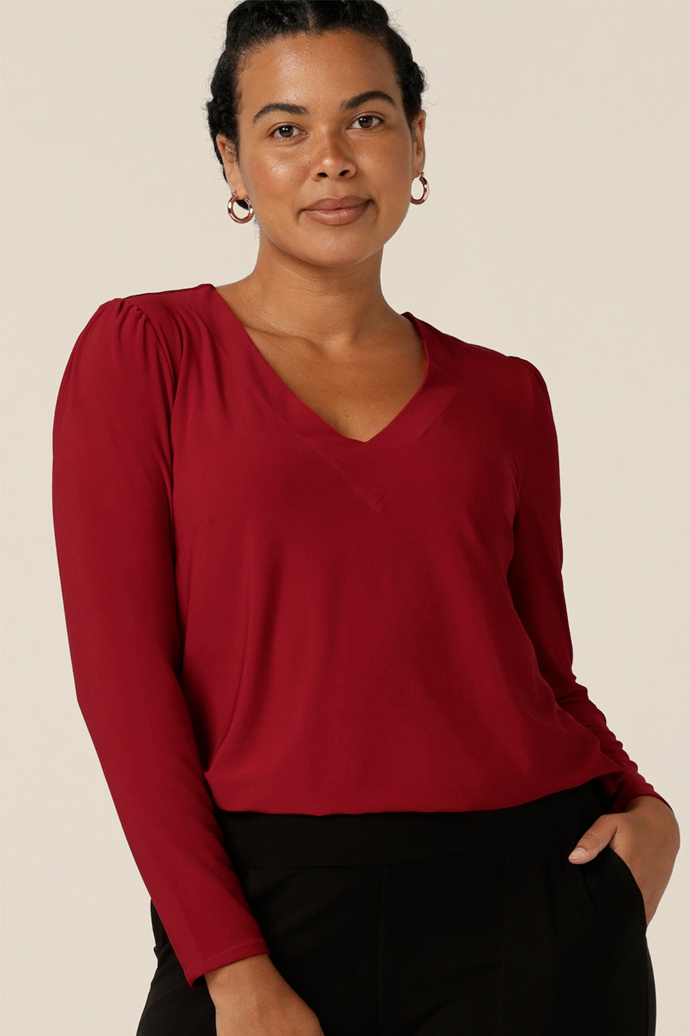 A size 12, curvy woman wears a V neck jersey top in flame red jersey. With long sleeves, this top is a good autumn/winter top, perfect for winter layering and styling under workwear jackets.