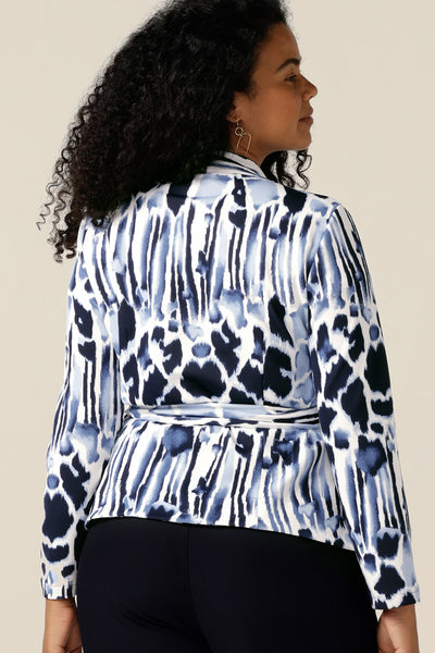 A size 12 curvy woman wears a wrap-over jacket in comfortable stretch jersey. Patterned in navy blue and white, this jacket has a V-neck, long sleeves and a belt tie. Designed as a work wear jacket and made in Australia, women of Australia and New Zealand, shop quality corporate jackets in sizes 8 to size 24 at Leina and Fleur.