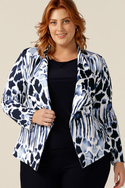 A size 18, plus size woman wears a comfortable work jacket in navy and white. Open-fronted, this soft tailored jacket has a tie belt and long sleeves. Worn with slim-leg navy pants, this jacket is a good workwear jacket for corporate and smart-casual business wear.