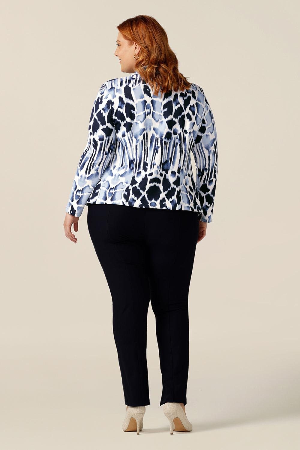 A size 18, plus size woman wears a comfortable work jacket in navy and white. Open-fronted, this soft tailored jacket has a tie belt and long sleeves. Worn with slim-leg navy pants, this jacket is a good workwear jacket for corporate and smart-casual business wear.