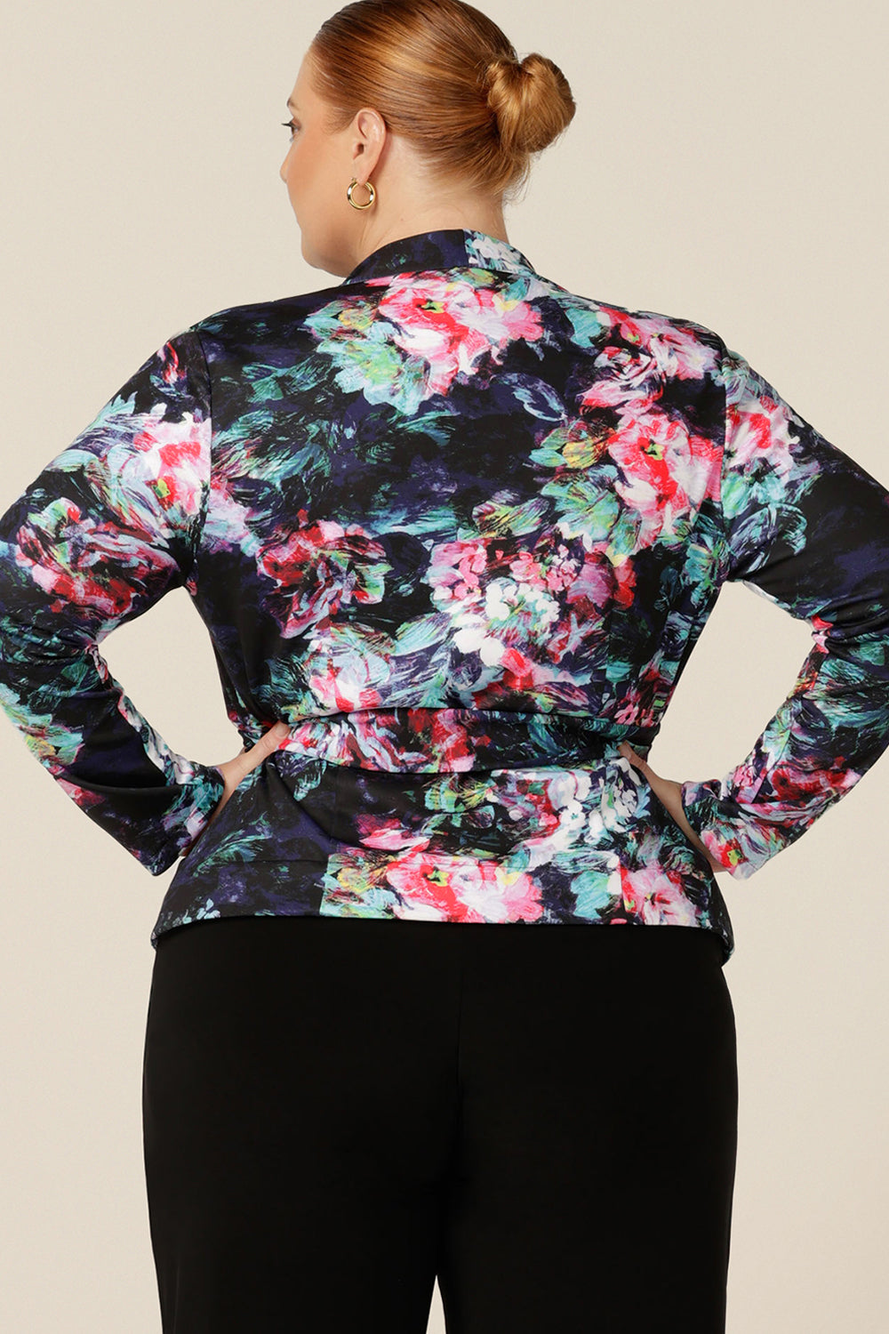 Back view of a size 18, fuller figure woman wearing a comfortable work jacket in abstract floral print on a black base. This soft tailoring jacket has a tie belt, soft collar and long sleeves. Made in Australia in sizes 8-24, shop this work jacket with free shipping to New Zealand.