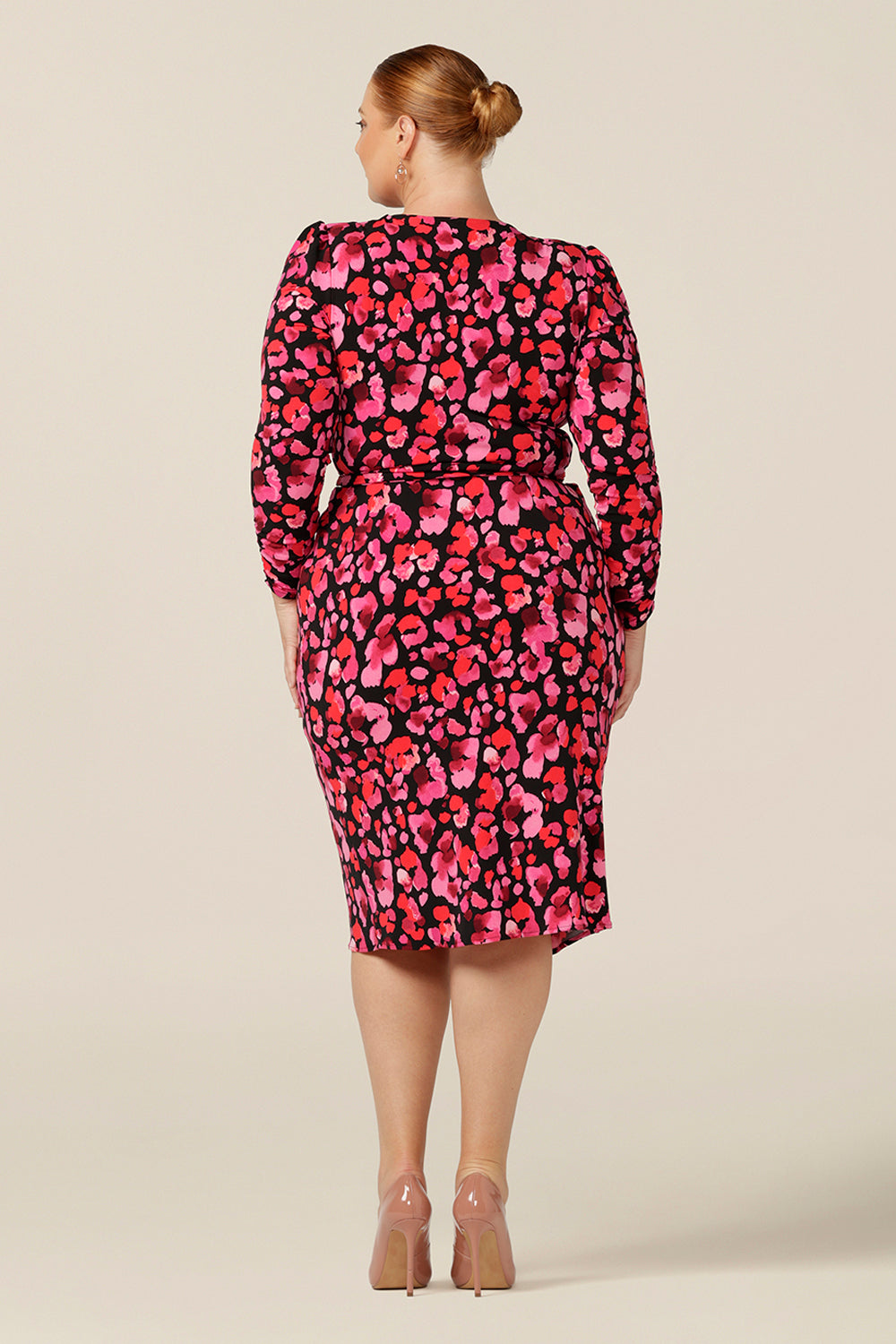 Back view of a  fuller figure, size 18 woman wearing a jersey wrap dress with long sleeves and a tulip skirt. Made in Australia and available to shop online in Australia and New Zealand, this wrap dress features a red floral print on a black base and can be worn for work wear or as an event dress for date night style.
