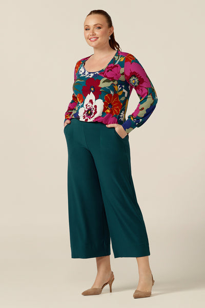 A curvy size 12 woman wears a scoop neck jersey top with long bishop sleeves. Australian-made, this quality top is designed for work and casual wear and shown tucked in to wide-leg work pants.