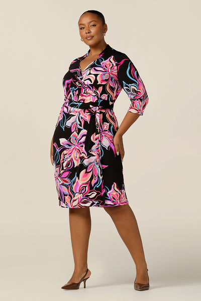 A size 18 woman wears a bright-coloured floral print jersey wrap dress by Australian and New Zealand women's clothing label, L&F. A good corporate dress, it features collared V-neck, 3/4 sleeves and a fitted knee-length skirt. Made in Australia, shop L&F corporate dresses in sizes 8 to size 24. 