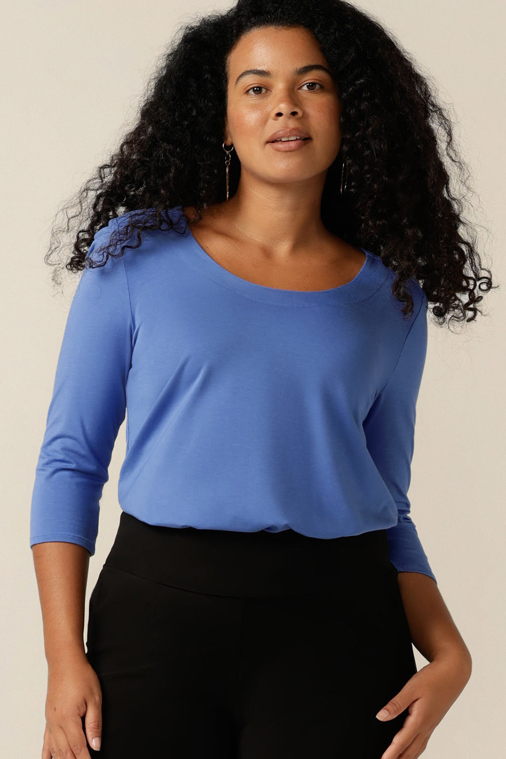 A curvy size 12 woman wears a blue bamboo jersey top. The top has a round neckline, 3/4 sleeves, and a curved shirttail hemline. Made in bamboo jersey, this top is made from sustainable, natural fibres that are lightweight and breathable and part of the movement towards eco-conscious fashion.