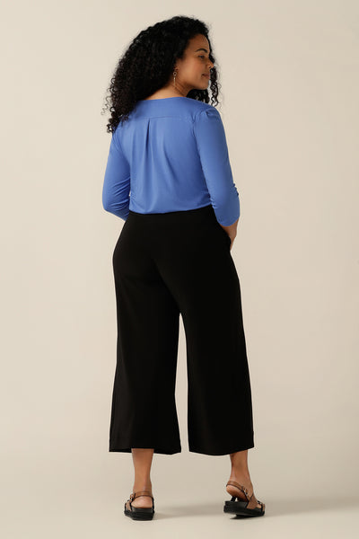 A curvy size, size 12 woman wears a blue bamboo jersey top. The top has a round neckline, 3/4 sleeves, and a curved shirttail hemline. Worn with black work wear pants, tuck in this bamboo jersey top and she becomes a smart-casual work wear top. Shop this top in size 12, as pictured, or select from the full women's clothing range of sizes 8 to 24. 