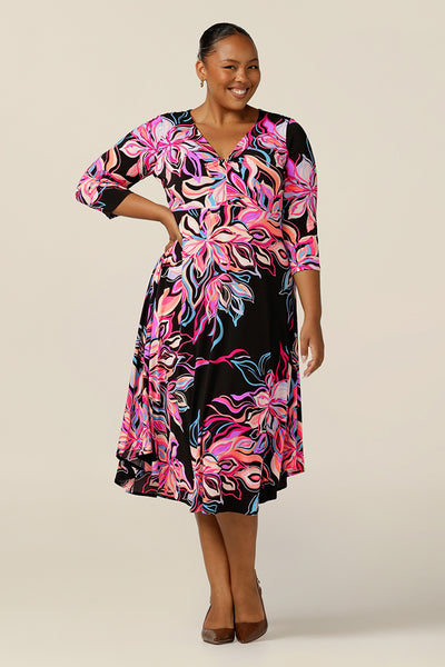 A size 18 woman wears a bright-coloured floral print jersey dress by Australian and New Zealand women's clothing label, L&F. this empire line dress features a V-neckline with twist detail, 3/4 sleeves and a full below-the-knee-length skirt. Made in Australia, shop L&F corporate dresses in sizes 8 to size 24.
