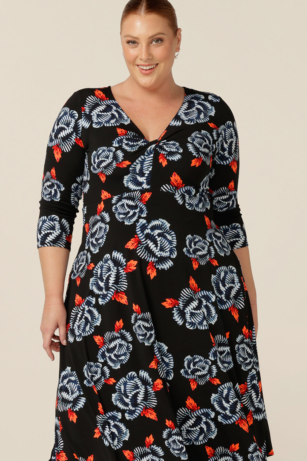Close up detail of twist front, empire line jersey dress by Australian and New Zealand women's clothing label, L&F. In a size 18, a woman wears a blue and orange floral print jersey dress by Australian and New Zealand women's clothing brand, L&F. this empire line dress features a V-neckline with twist detail, 3/4 sleeves and a full below-the-knee-length skirt. Australian-made, shop L&F workwear dresses in sizes 8 to size 24.