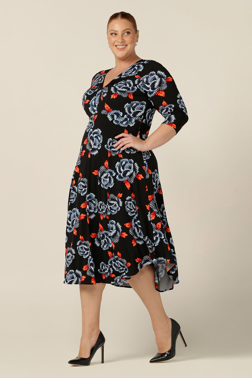 A size 18 plus size woman wears a blue and orange floral print jersey dress by Australian and New Zealand women's clothing brand, L&F. this empire line dress features a V-neckline with twist detail, 3/4 sleeves and a full below-the-knee-length skirt. Australian-made, shop L&F work dresses in sizes 8 to size 24.