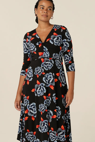 A size 12 woman wears a blue and orange floral print jersey dress by Australian and New Zealand women's clothing brand, L&F. this empire line dress features a V-neckline with twist detail, 3/4 sleeves and a full below-the-knee-length skirt. Made in Australia, shop L&F work dresses in sizes 8 to size 24.