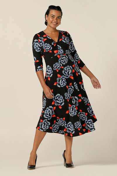 A size 12 woman wears a blue and orange floral print jersey dress by Australian and New Zealand women's clothing label, L&F. This empire line dress features a V-neckline with twist detail, 3/4 sleeves and a full below-the-knee-length skirt. Made in Australia, shop L&F corporate dresses in sizes 8 to size 24.