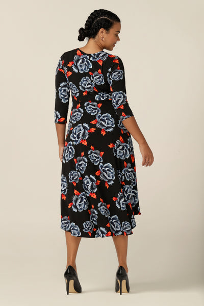 Back view of a size 12 woman wears a blue and orange floral print jersey dress by Australian and New Zealand women's clothing label, L&F. this empire line dress features a V-neckline with twist detail, 3/4 sleeves and a full below-the-knee-length skirt. Made in Australia, shop L&F work dresses in sizes 8 to size 24.