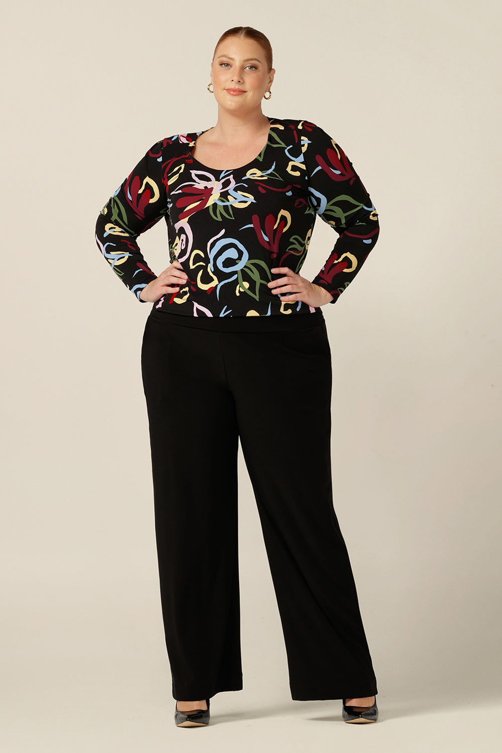 a round neck, long sleeve jersey top for plus size and fuller figure women, this workwear top features an abstract print with black base. Styled for the office, this comfortable top is worn with black straight-cut, wide leg, black pants.