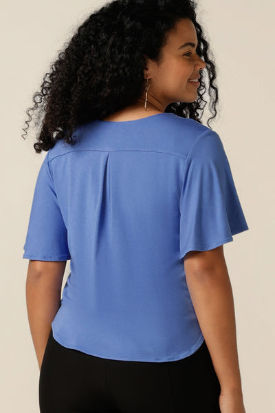 A size 12 curvy woman wears a blue bamboo jersey top with a V-neck and short flutter sleeves. It is a lightweight and breathable top thanks to its natural and sustainable bamboo fibres, and being made in Australia, it is part of L&Fs move towards greater sustainability and eco-conscious fashion.