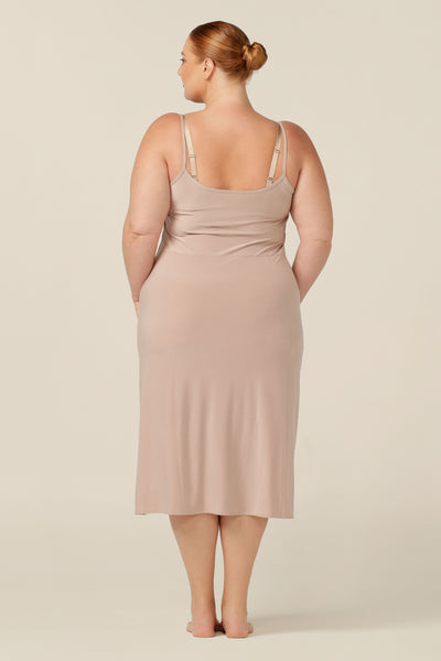 A fuller figure woman wears a flesh-coloured, midi-length, reversible slip in slinky jersey. Worn with a V neck to the front, and scoop neck to the back. With a skirt length finishing below the knee, this midi slip gives a smooth layer under dresses and skirts.