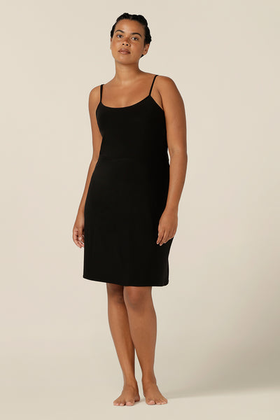 A size 12 woman wears a mini-length, reversible slip in black, slinky jersey fabric. The slip has thin straps and is worn with a scoop neck to the front. The slip skirt finishes above the knee to layer under dresses and separates. Slip dress in plus size