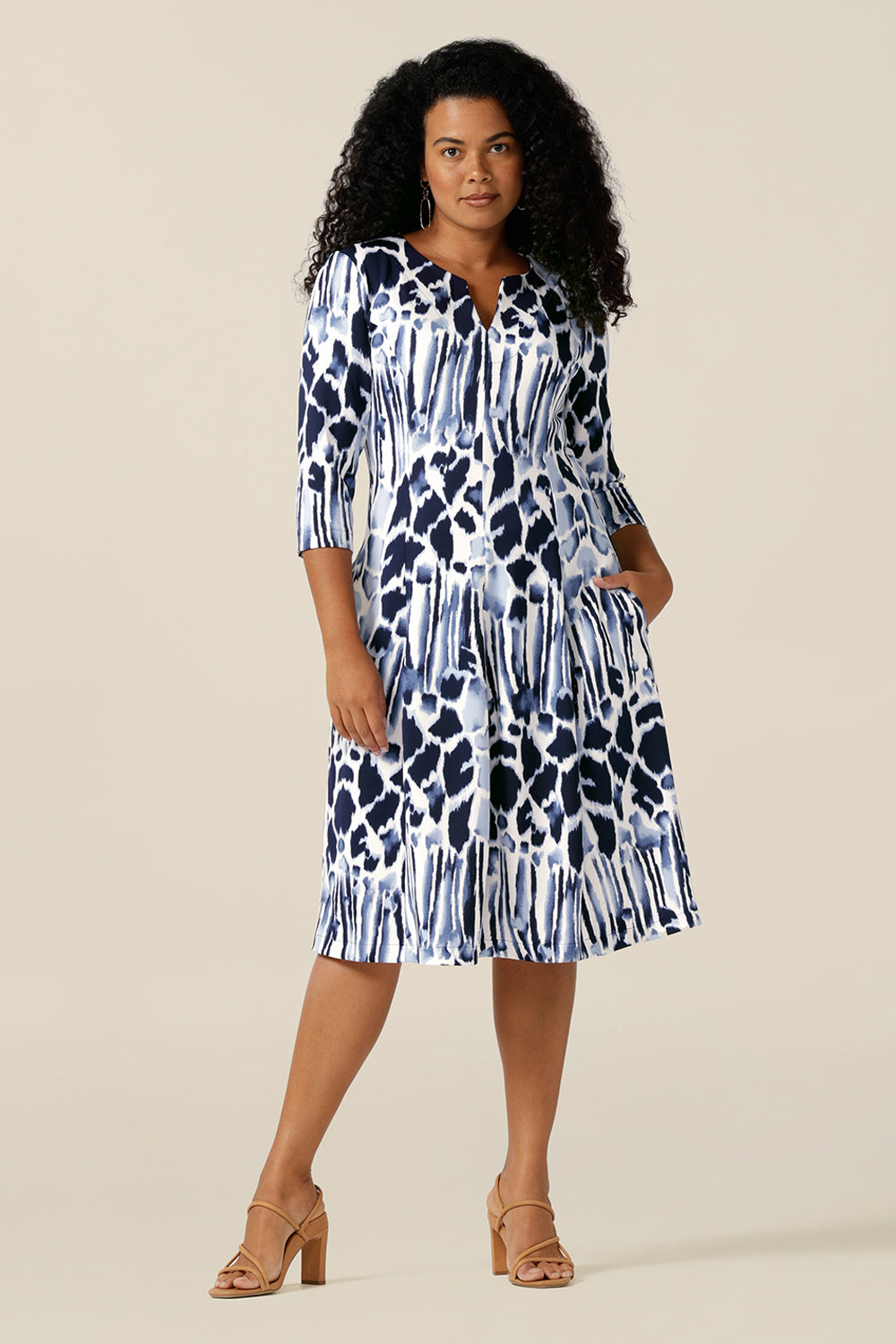 a woman wears a panelled work dress in navy and white jersey. The fitted jersey dress has a round neck with V opening, side pockets and below-the-knee length skirt. Women of Australia and New Zealand, in sizes 8 to size 24, buy this good corporate dress for a chic work wear outfit.