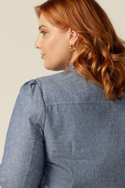 size 18 woman wearing a soft tailored jacket in cotton-linen blend Chambray fabric. The jacket is open-fronted and has long sleeves. This jacket is styled with a white shirt and matching Chambray tailored, cropped-length pants to give a work wear look. Jacket, shirt and pants are made in Australia for petite to plus size women.