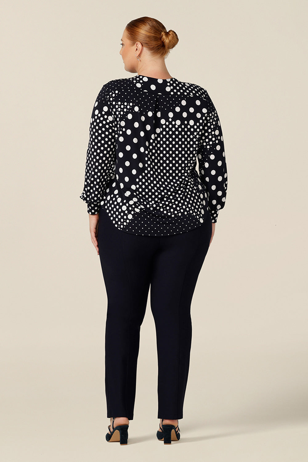 Back view of a size 18, plus size woman wearing a long sleeve, V-neck top in navy and white polka dot print jersey. A good top for work and casual wear, shop this top online in an inclusive size range of 8-24.