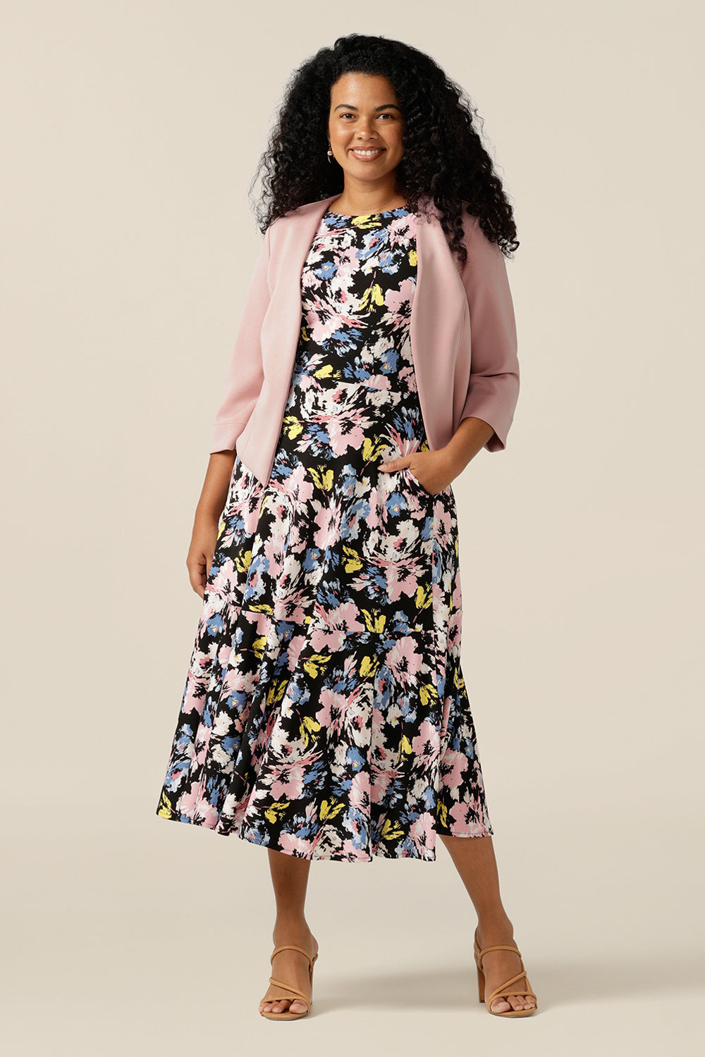 A size 12 curvy woman wears an open-front, collarless jacket with 3/4 sleeves. Made from pink modal jersey, this comfortable jacket is sustainably-made using natural fibres and eco-conscious production. A good sustainable corporate jacket, the Rainy Jacket is worn with a vintage floral print jersey dress.