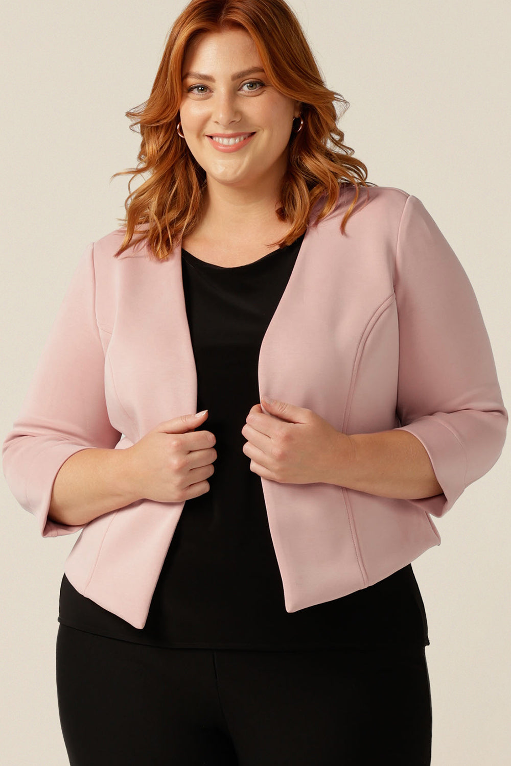 a size 18, plus size woman wears a collarless, open-front pink jacket with 3/4 sleeves. Made in Australia from stretch modal, a sustainable natural fibre, this is an eco-conscious quality corporate jacket. The sustainably-produced women's jacket is worn with a black jersey top and comfortable black work trousers.
