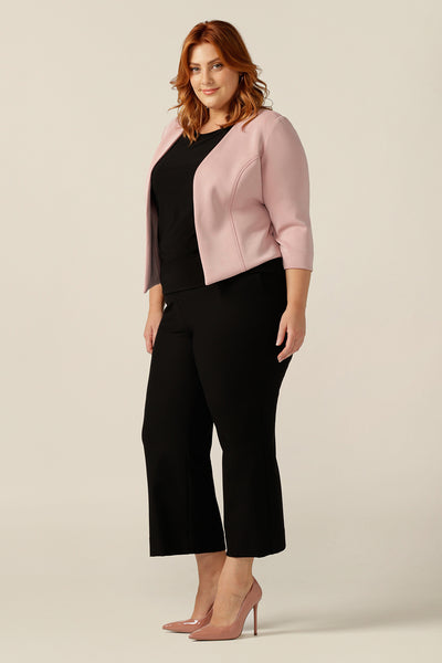 a size 18, plus size woman wears a collarless, open-front pink jacket with 3/4 sleeves. The pink jacket is worn with a black top and black trousers as a complete work wear outfit. Made in Australia from stretch modal, a sustainable natural fibre, this is an eco-conscious quality corporate jacket.