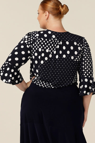 Back view of a comfortable workwear top for plus size and fuller figure women. This V-neck top with fluted 3/4 sleeves comes in a navy and white polka dot print.
