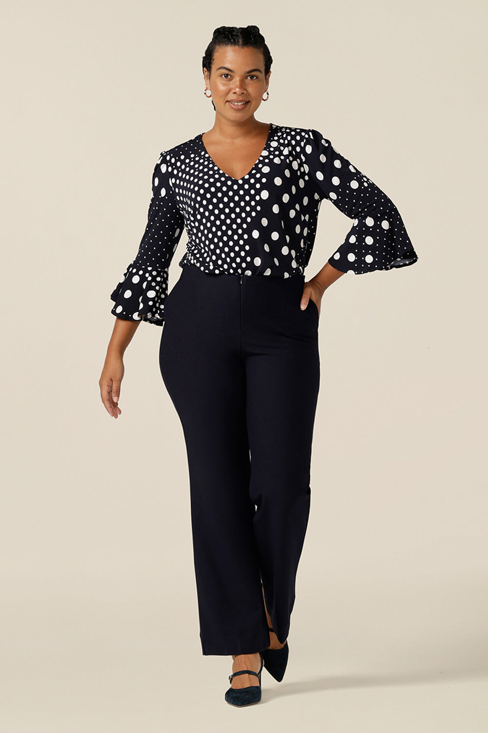 A women's workwear top in navy and white polka dot print. Worn with navy, bootcut flared leg trousers, this top features a V neckline and 3/4 sleeves with fluted cuffs. Shop this Australian-made top in petite to plus size women.